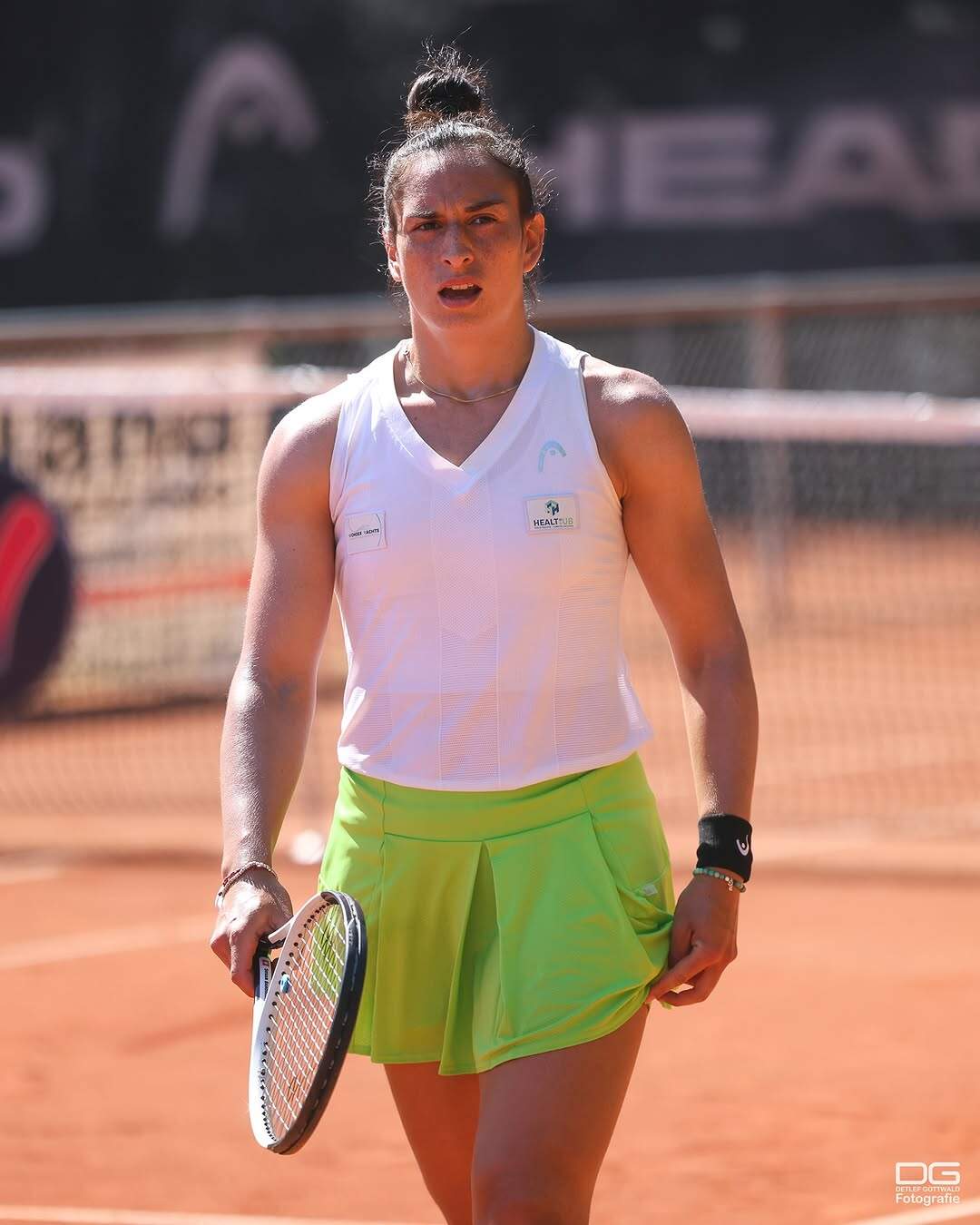 Spielerin in weiß und Neongrün auf dem Sandplatz